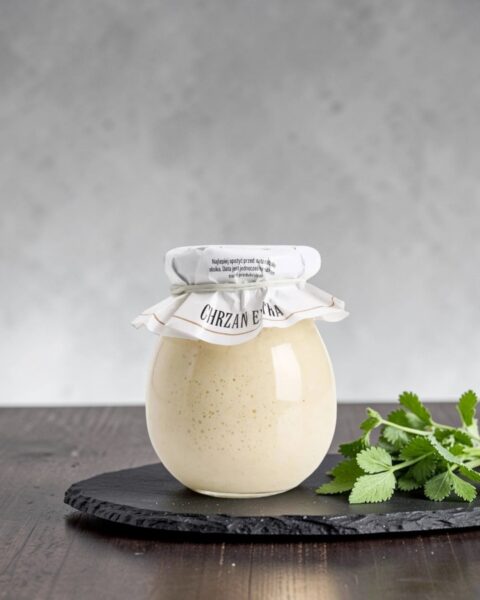 Chrzan extra Stara Wędzarnia - na czarnym kamiennym talerzu, drewniany stol, szare cementowe tlo, zielone ziola