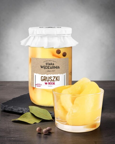 Gruszki w occie Stara Wędzarnia - na czarnym kamiennym talerzu, drewniany stol, szare cementowe tlo, zielone ziola