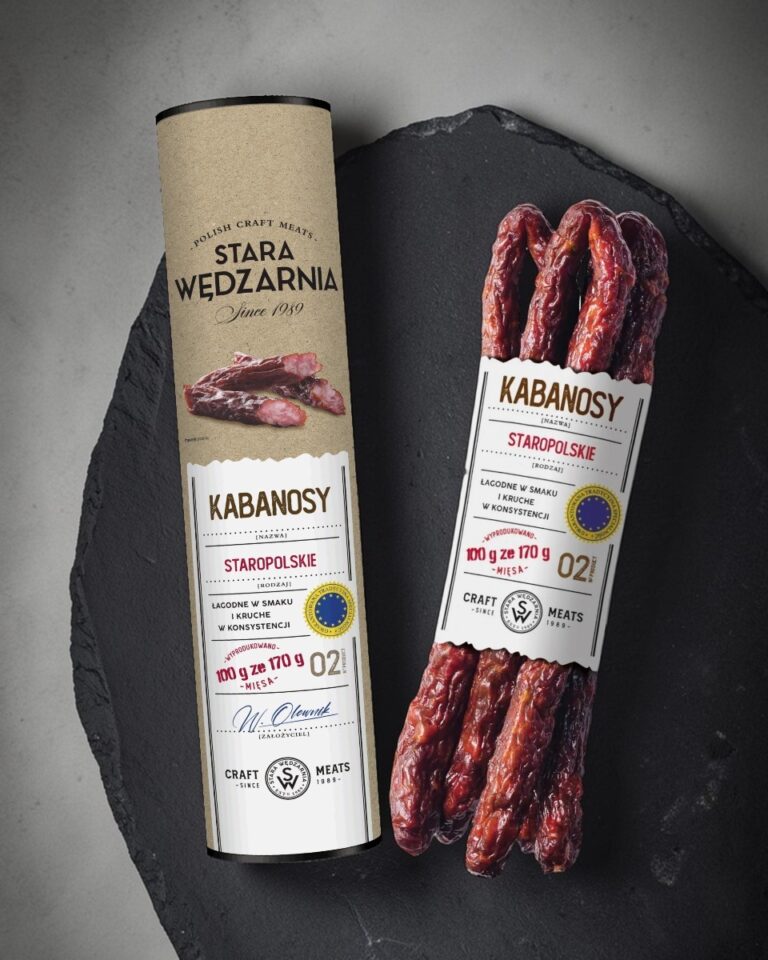 Kabanosy Staropolskie GTS Tuba Stara Wędzarnia - na czarnym kamiennym talerzu, drewniany stol, szare cementowe tlo, zielone ziola