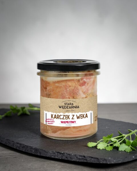 Karczek z weka wieprzowy Stara Wędzarnia - na czarnym kamiennym talerzu, drewniany stol, szare cementowe tlo, zielone ziola