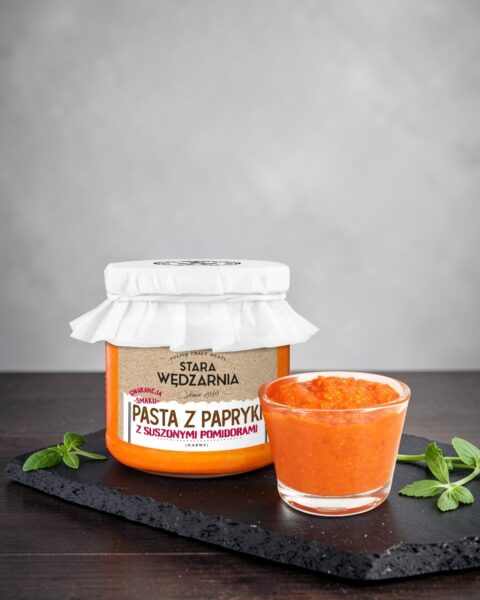 Pasta z papryki z suszonymi pomidorami Stara Wędzarnia - na czarnym kamiennym talerzu, drewniany stol, szare cementowe tlo, zielone ziola