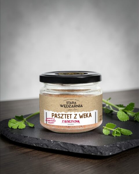 Pasztet z weka z dziczyzną Stara Wędzarnia - na czarnym kamiennym talerzu, drewniany stol, szare cementowe tlo, zielone ziola