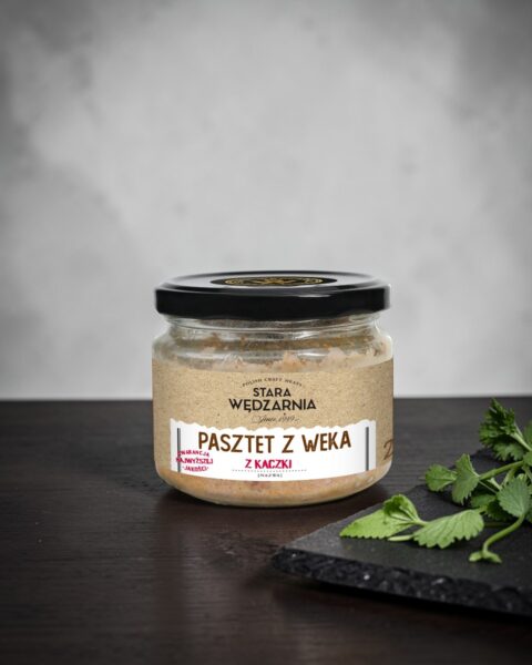 Pasztet z weka z kaczki Stara Wędzarnia - na czarnym kamiennym talerzu, drewniany stol, szare cementowe tlo, zielone ziola