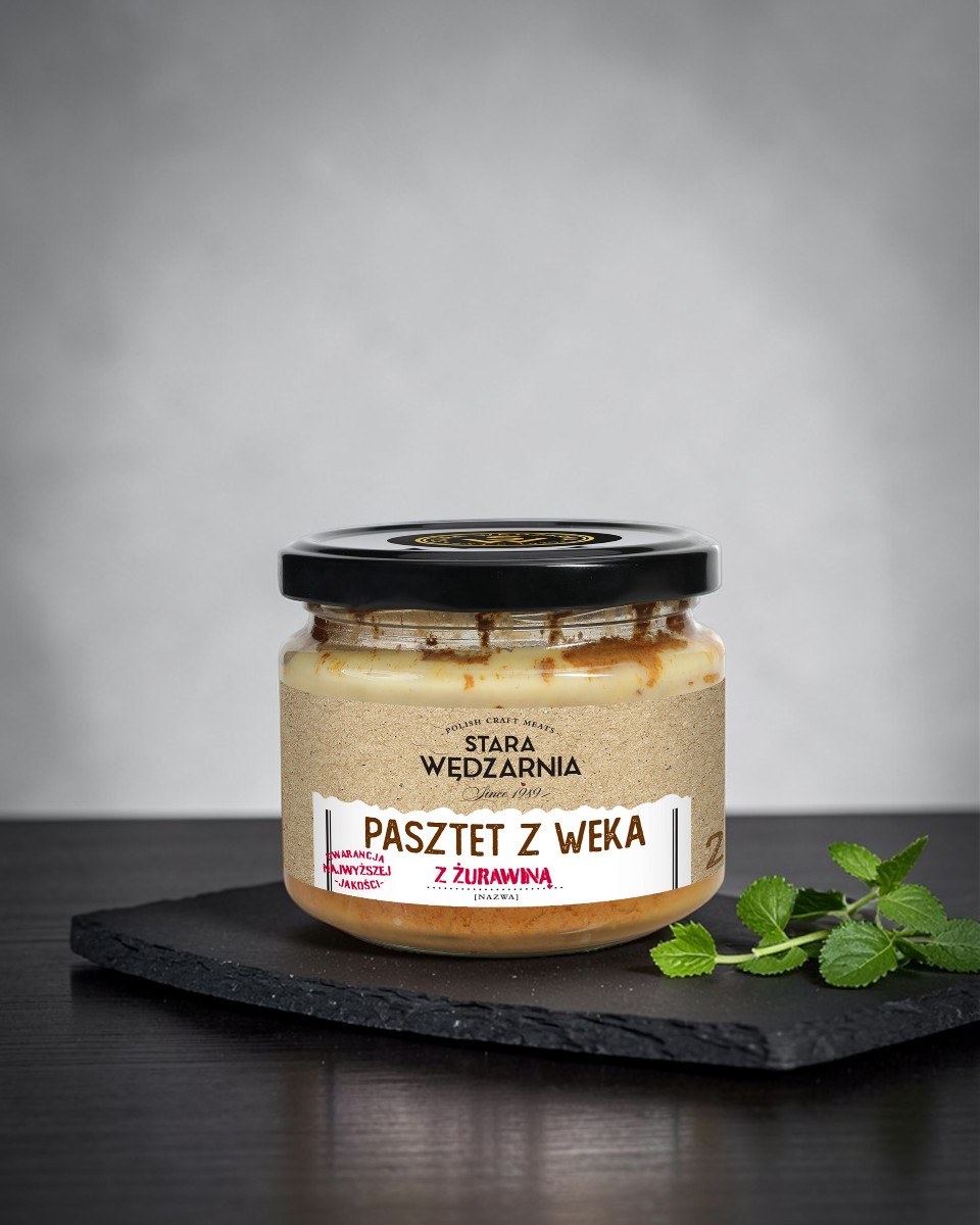 Pasztet z&nbsp;weka z&nbsp;żurawiną Stara Wędzarnia - na&nbsp;czarnym kamiennym talerzu, drewniany stol, szare cementowe tlo, zielone ziola