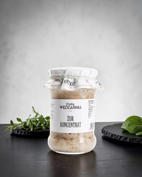 Żur polski Stara Wędzarnia - na czarnym kamiennym talerzu, drewniany stol, szare cementowe tlo, zielone ziola