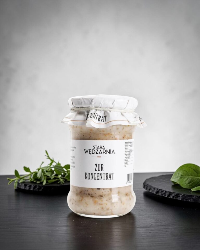 Żur polski Stara Wędzarnia - na czarnym kamiennym talerzu, drewniany stol, szare cementowe tlo, zielone ziola